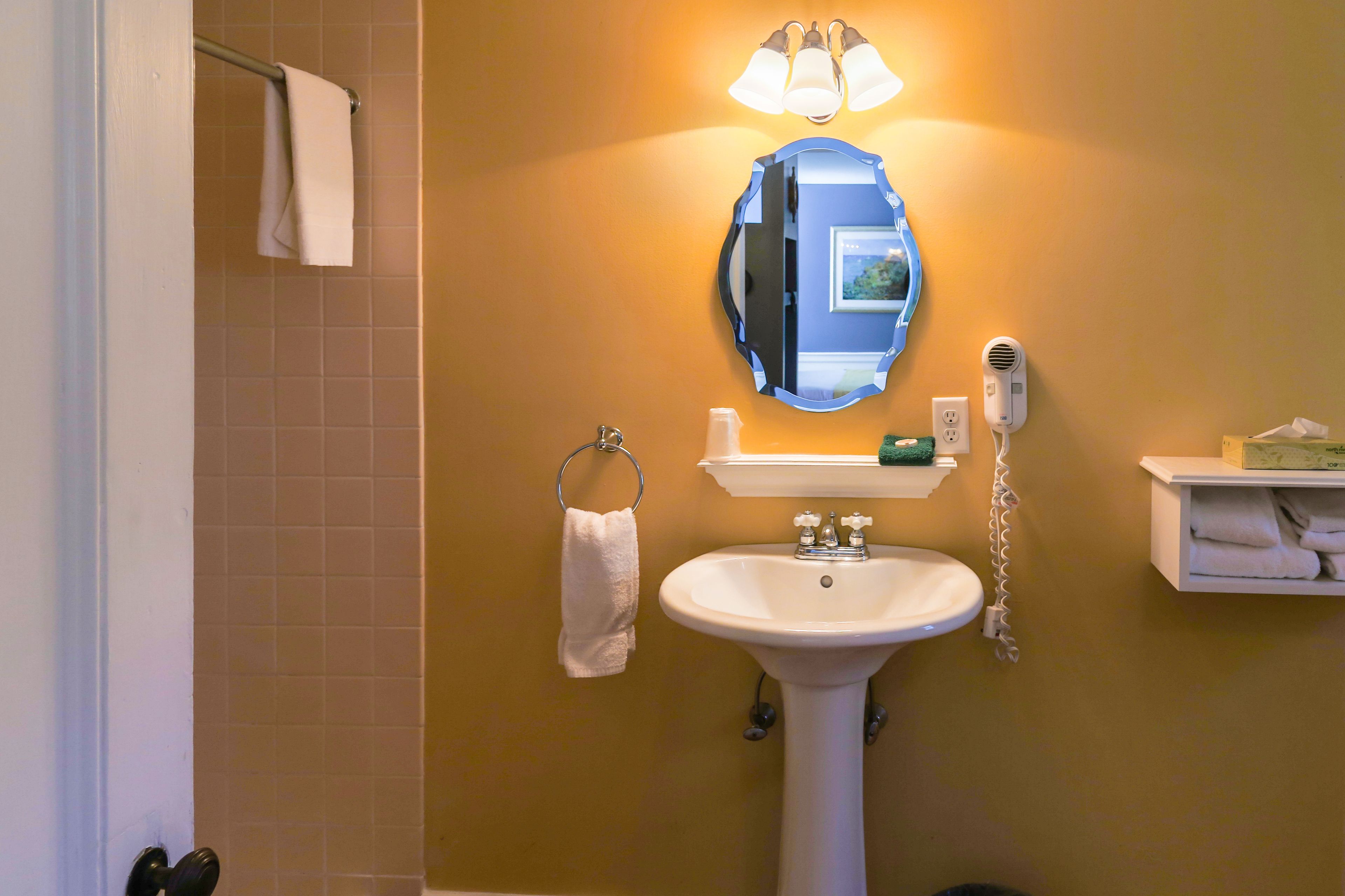 Ein Badezimmer mit Waschbecken, Spiegel, Handtuchhalter und einem an der Wand befestigten Föhn.