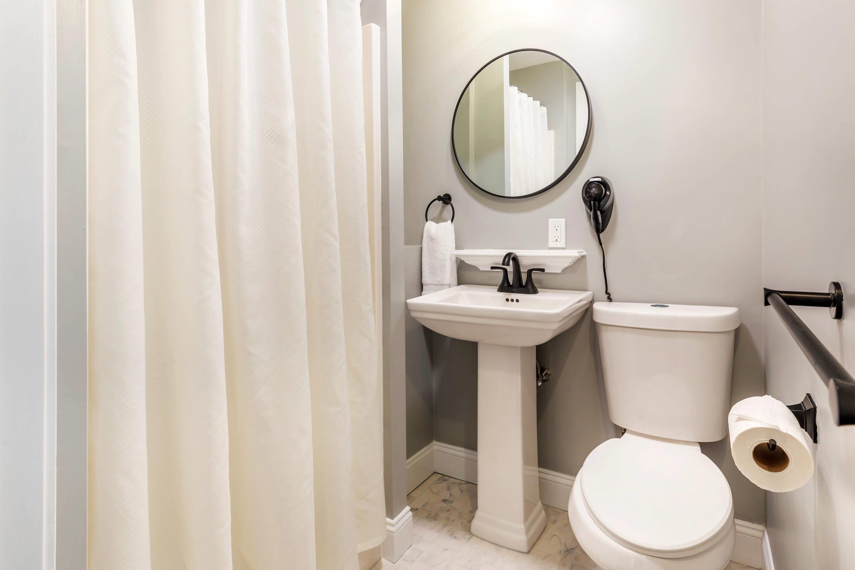 A bathroom with a pedestal sink, a toilet, a mirror, and a towel rack.