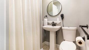 A bathroom with a pedestal sink, a toilet, a mirror, and a towel rack.