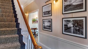 A staircase with a patterned carpet and wooden handrail, leading to a room with framed black and white photographs on the wall. - Essex Street Inn & Suites, an Ascend Collection Hotel (Newburyport)