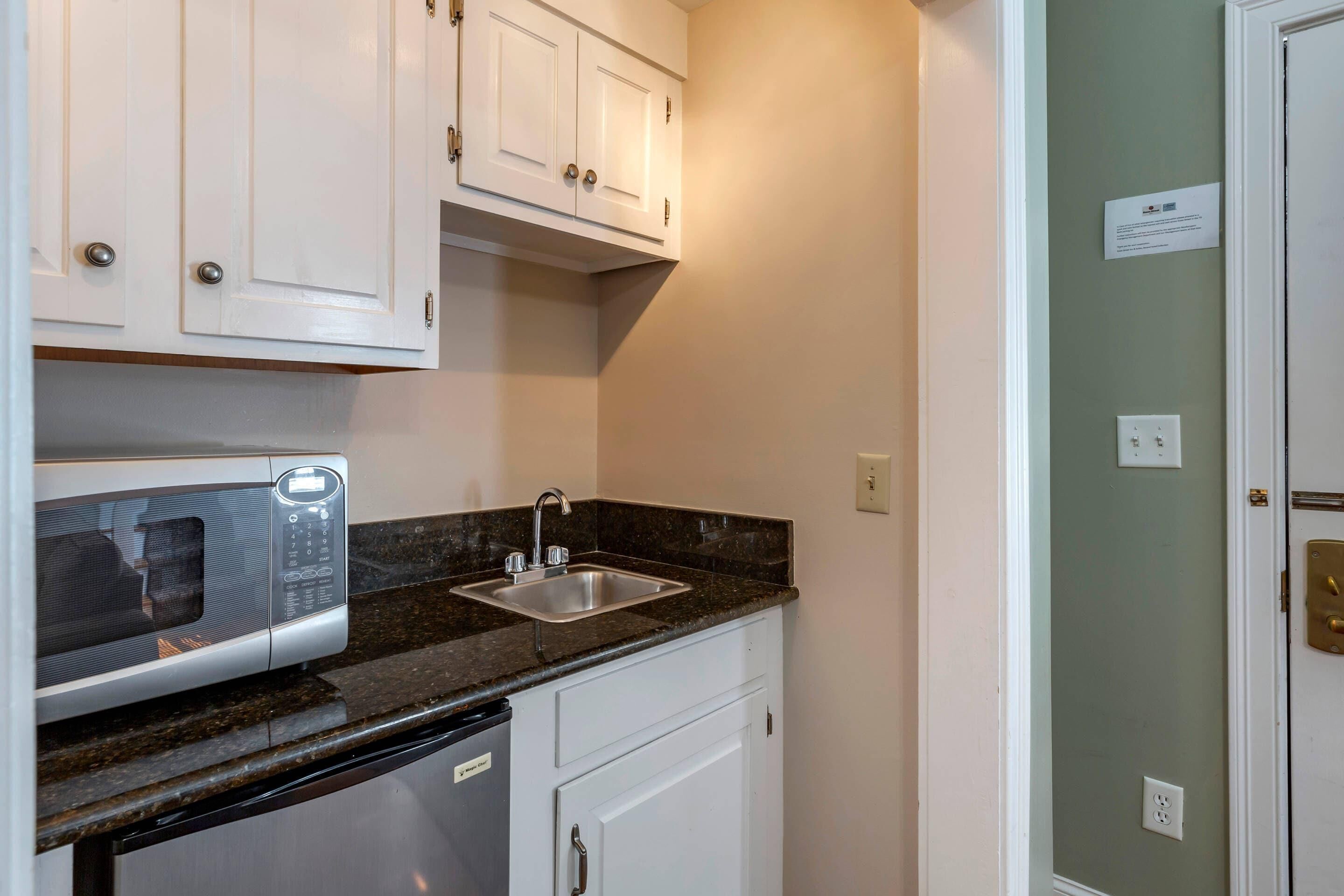 A compact kitchen with a built-in microwave, a sink, and white cabinetry.