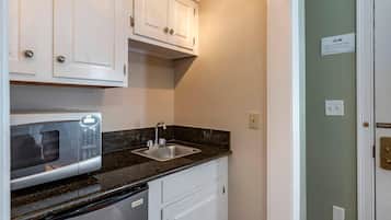 A compact kitchen with a built-in microwave, a sink, and white cabinetry.