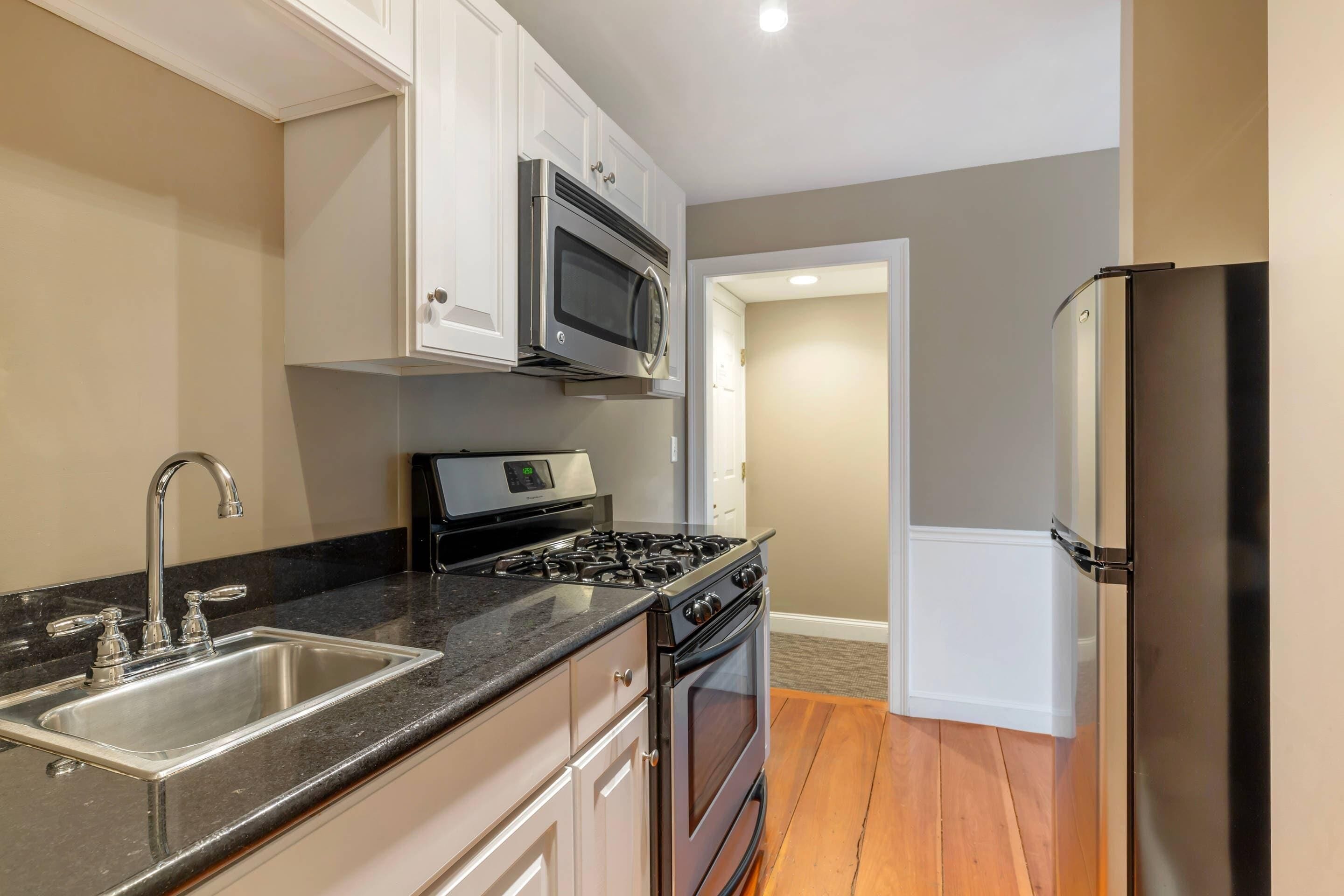 A kitchen with a stainless steel sink, a microwave, a stove, and a refrigerator.