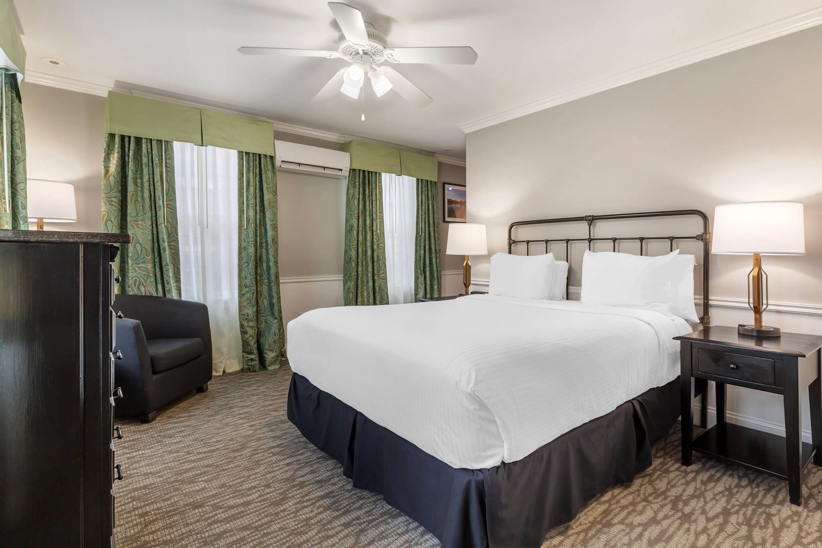 A hotel room with a large bed, two bedside lamps, a ceiling fan, a desk, and a chair.