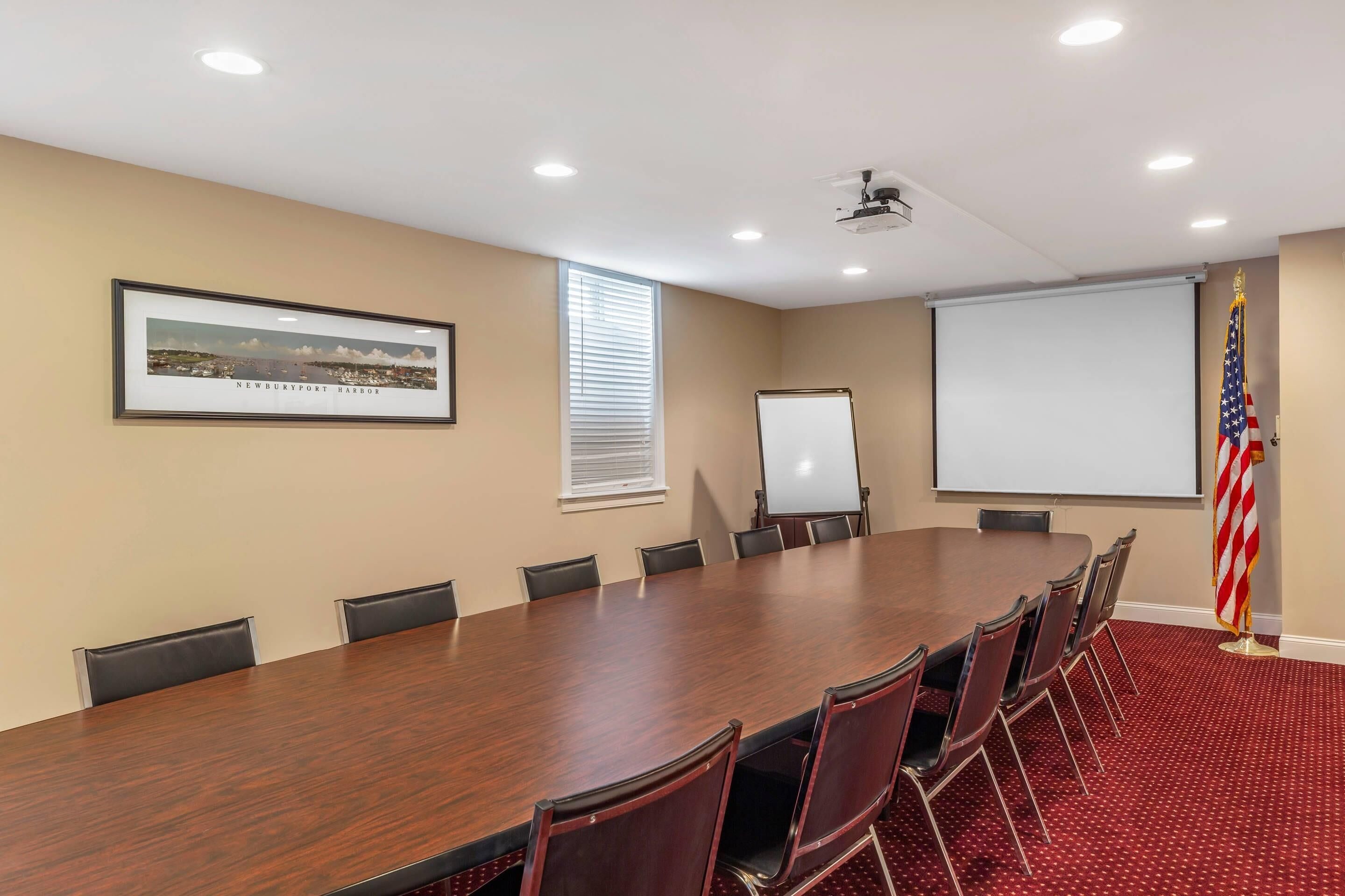 Un salón de conferencias con una larga mesa, sillas, una pantalla de proyector, una pizarra y una bandera estadounidense.
