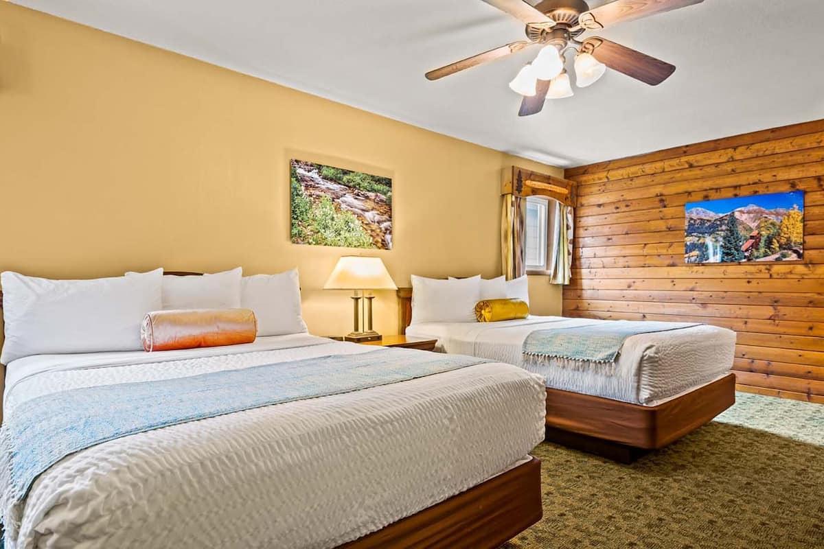 A hotel room with two beds, a ceiling fan, and wooden paneling on the walls.