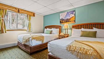 A hotel room with two beds, a window with curtains, a painting on the wall, and a lamp on the nightstand.