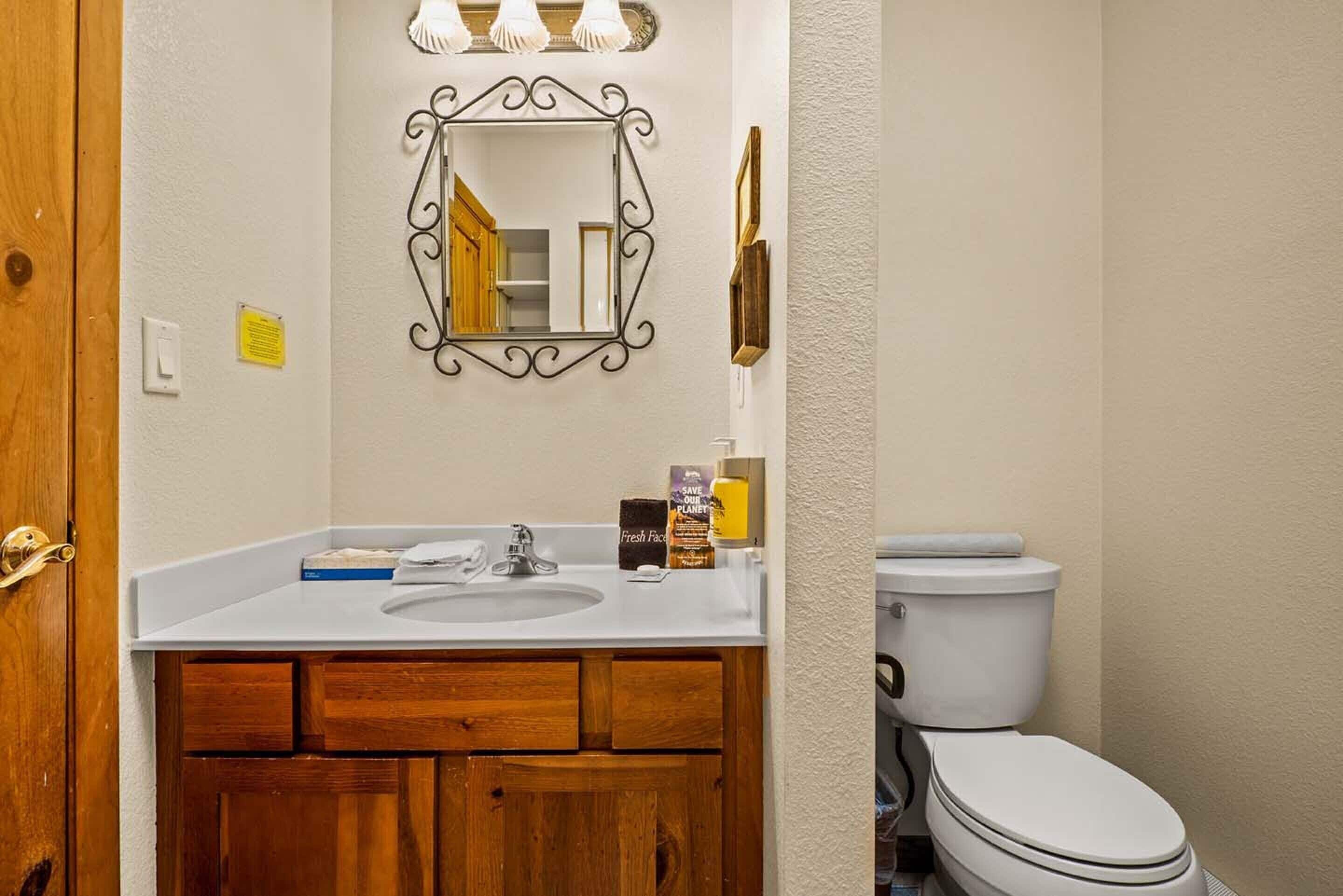 A bathroom with a wooden vanity, a white sink, a mirror with a decorative frame, and a toilet.