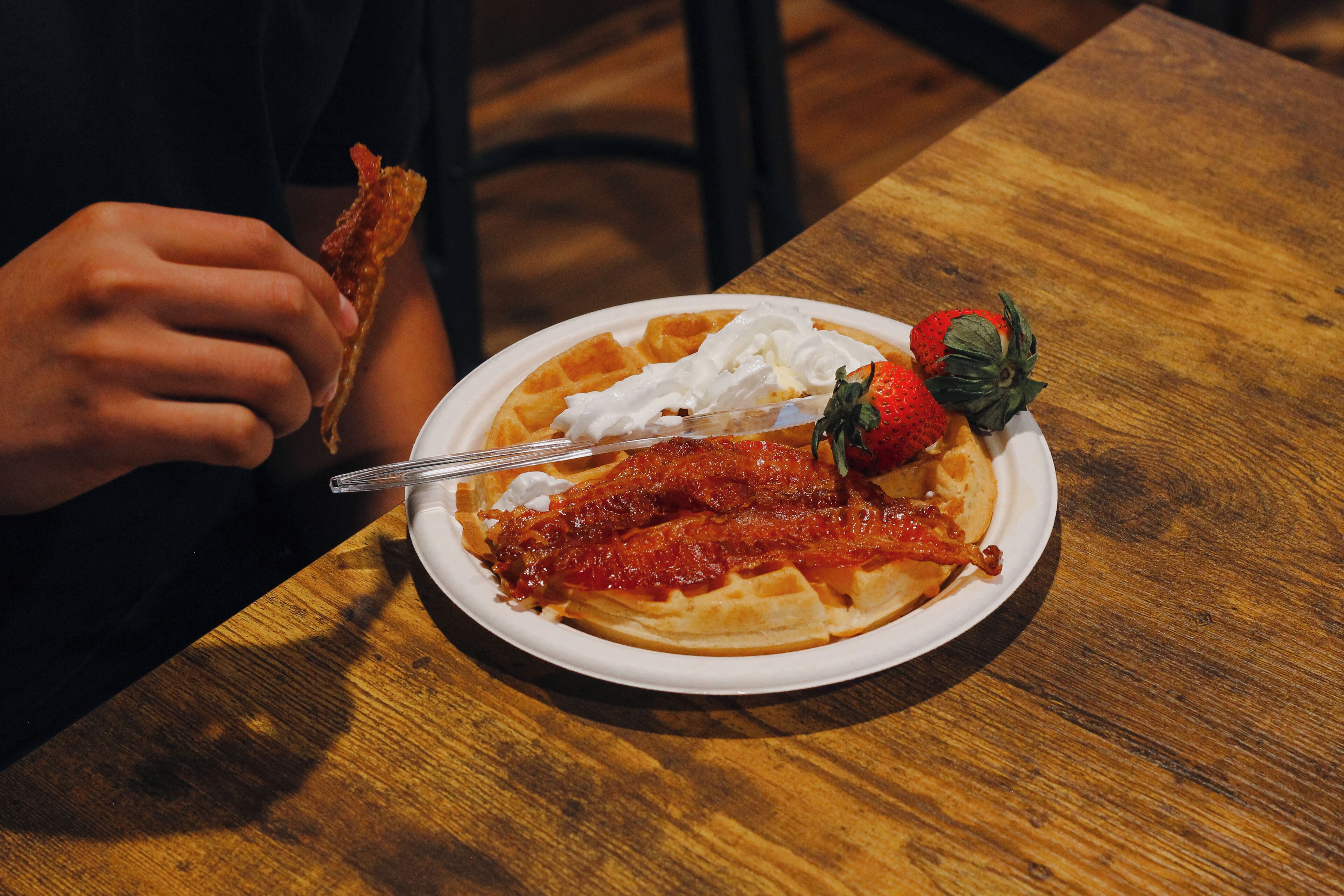 A plate of food with a waffle, whipped cream, and a strawberry on a wooden table.