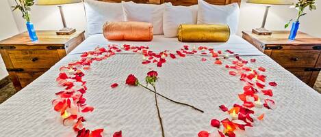 A neatly made bed with rose petals arranged in a heart shape and a single rose on the bed.