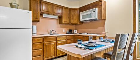 Una cocina con armarios de madera, un refrigerador blanco, un microondas y una mesa de comedor con sillas.