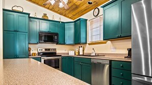 Una cocina con gabinetes verde azulado, electrodomésticos de acero inoxidable y encimera de granito.