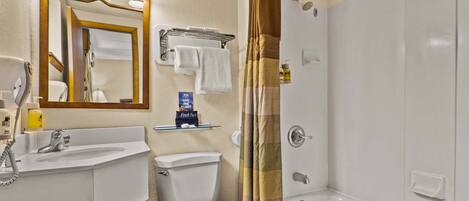 A bathroom with a sink, toilet, and shower. There is a mirror above the sink and a towel rack.