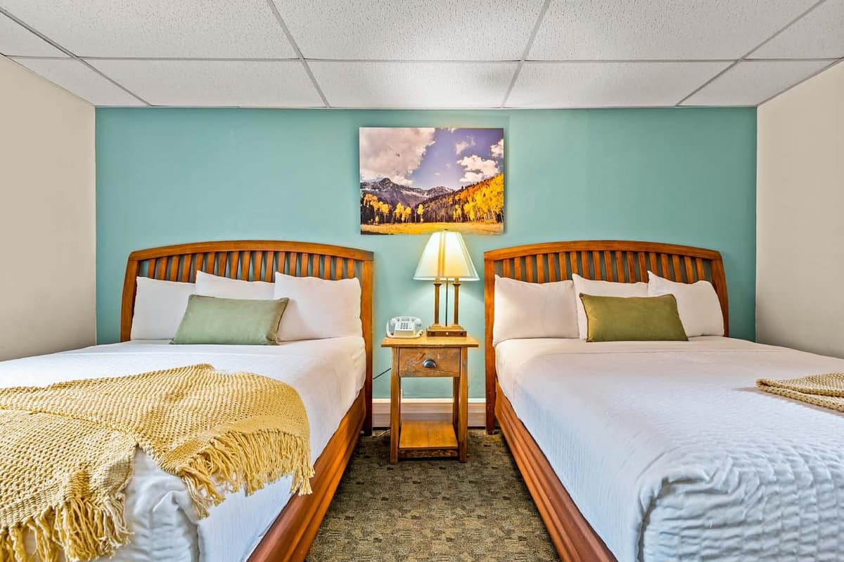 A hotel room with two beds, a nightstand with a lamp, and a painting on the wall.