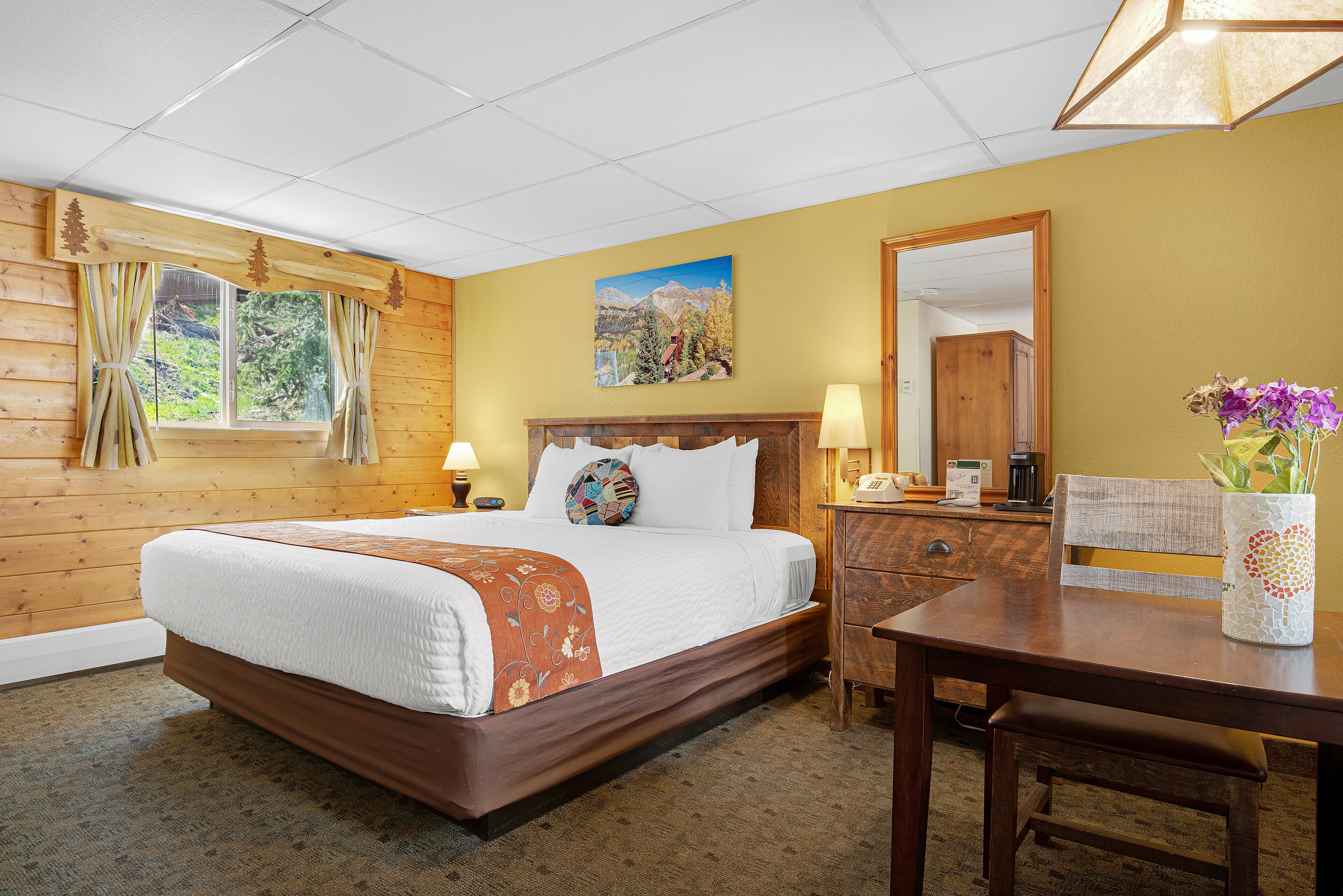 A hotel room with a wooden bed, a nightstand, a desk, and a mirror.