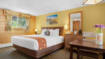 A hotel room with a wooden bed, a nightstand, a desk, and a mirror.