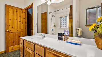 A bathroom with a wooden door, a white sink, a mirror, and a shower.