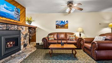 A cozy living room with a fireplace, leather sofas, a coffee table, and a ceiling fan.