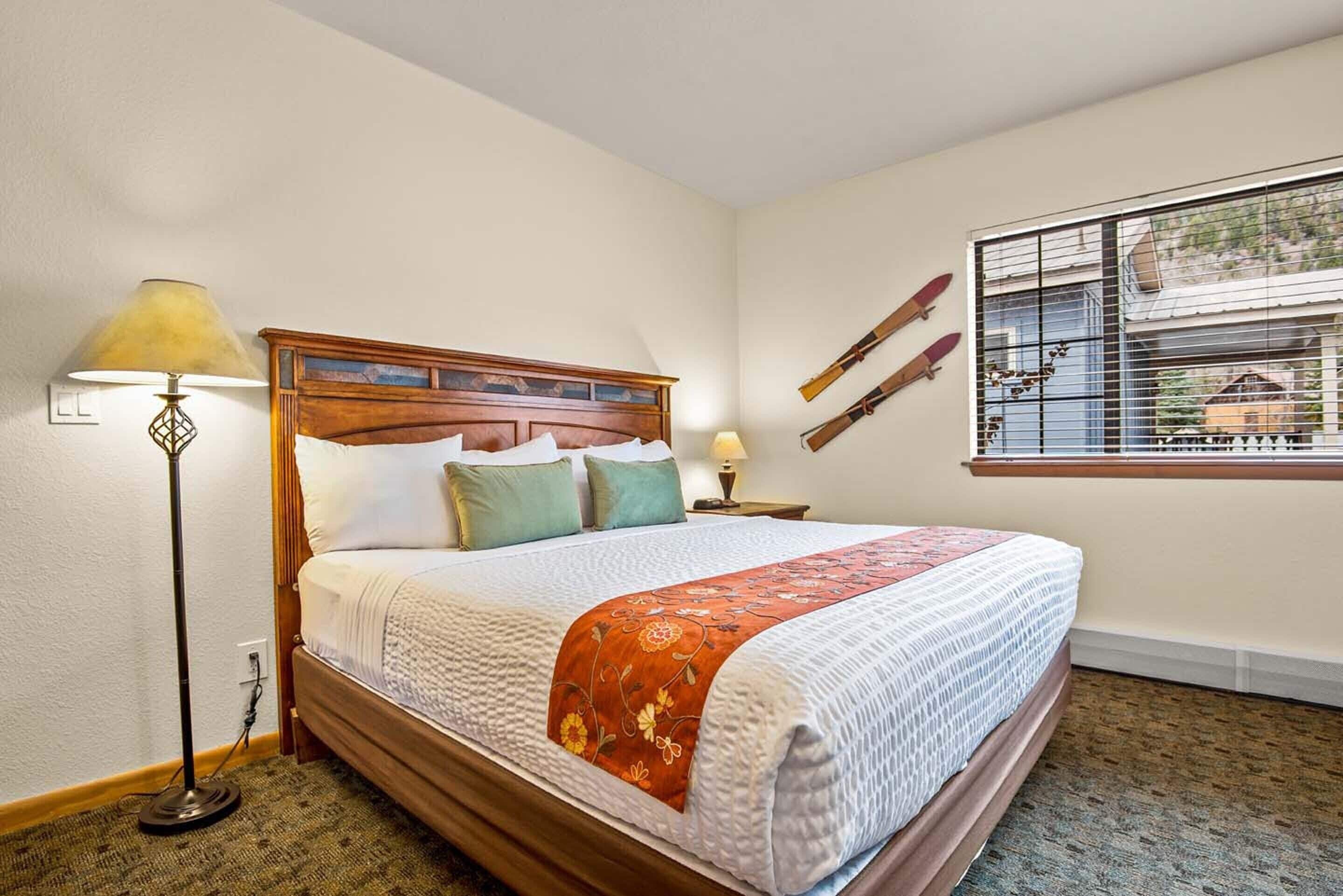 A neatly made bed with a wooden headboard, a bedside lamp, and a window with a view of the outside.