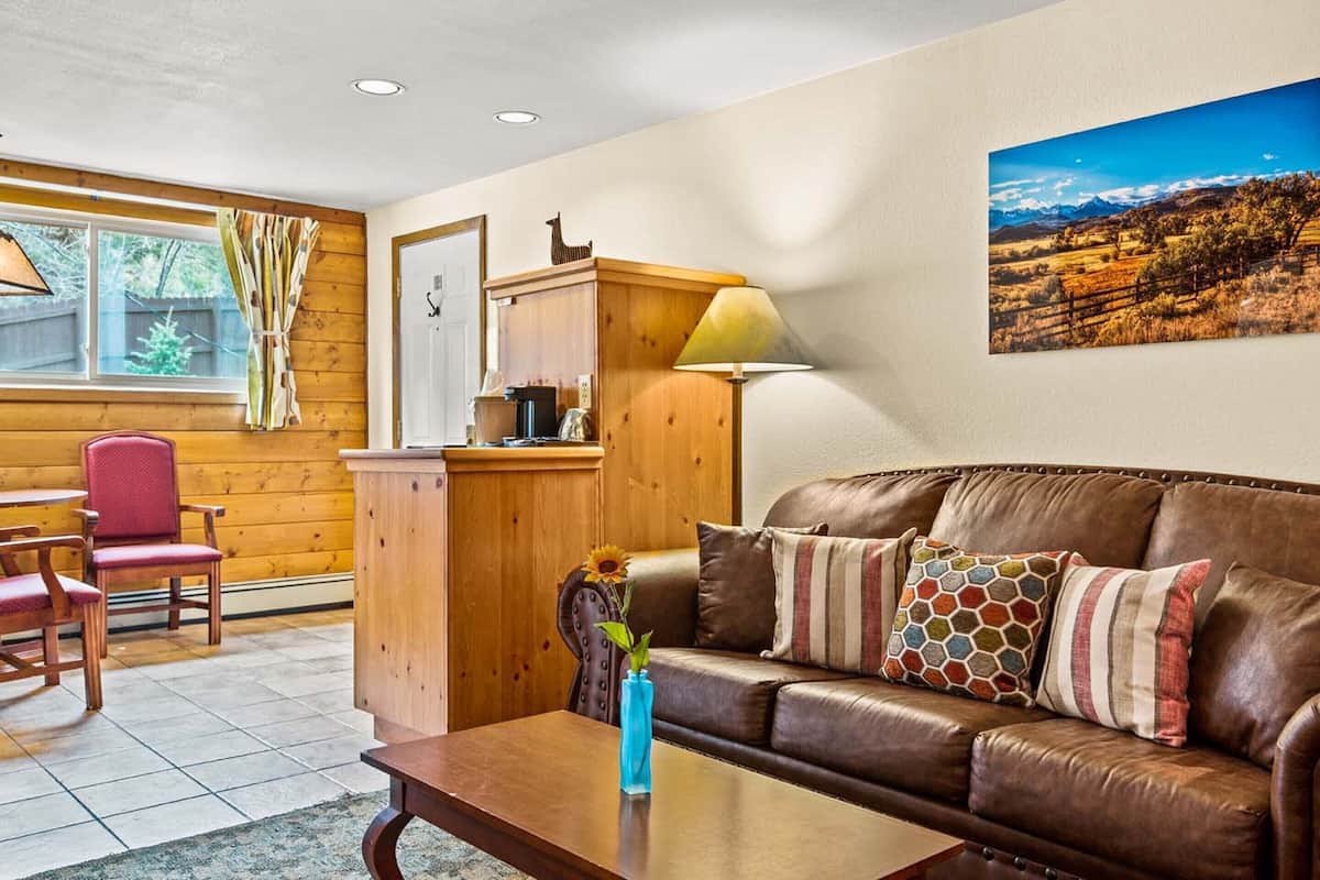 A cozy living room with a brown leather sofa, a wooden cabinet, a red chair, and a painting of a landscape on the wall.