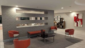 A modern interior with a herringbone-patterned wall, a glass coffee table, red upholstered chairs, and a bookshelf. - Sonesta Essential Columbus (Columbus)