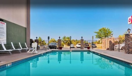 A swimming pool with lounge chairs, a stone wall, and a fence.