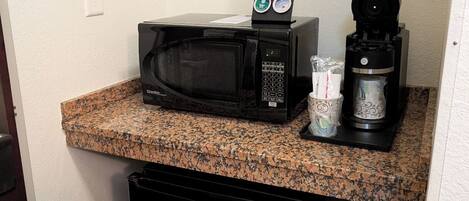 A compact kitchenette with a black microwave, a coffee maker, and a small refrigerator.