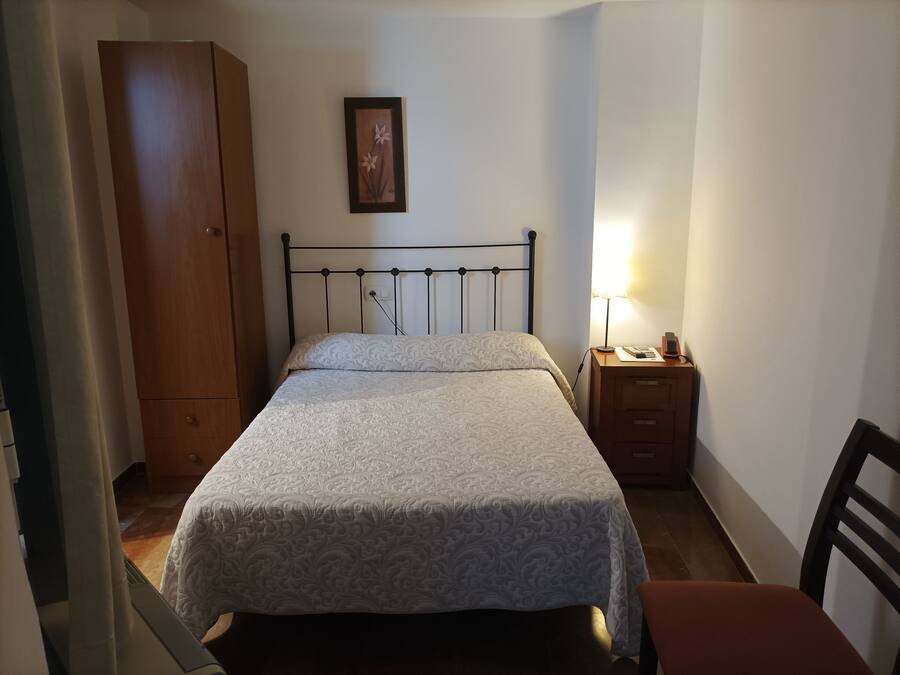 A bedroom with a bed, a nightstand, a lamp, a wardrobe, and a framed picture on the wall.
