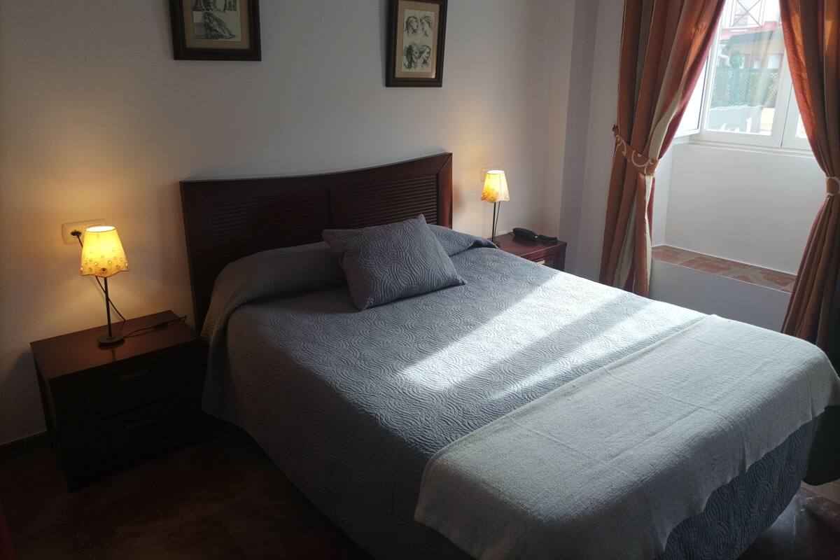 Un lit bien fait, recouvert d’une couverture à motifs, avec deux lampes de chevet et des œuvres d’art encadrées accrochées au mur.