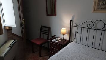 A hotel room with a bed, a chair, a desk with a lamp, a telephone, and a radiator.