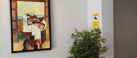 A hallway with a framed painting, a potted plant, and a security camera.