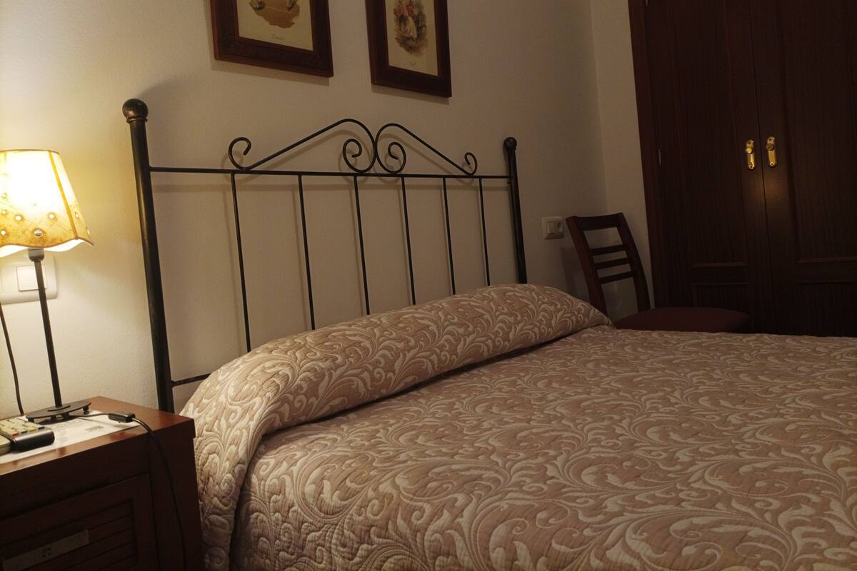 Une chambre à coucher avec un lit, une table de chevet, une lampe, une chaise et deux tableaux encadrés accrochés au mur.
