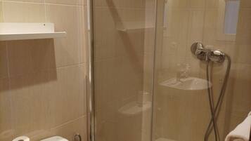 A bathroom with a glass-enclosed shower, a toilet, and a towel hanging on the shower door.