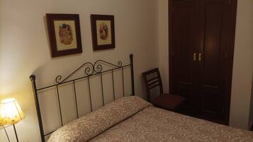 A neatly made bed with a patterned bedspread, a bedside table with a lamp, and two framed pictures on the wall.