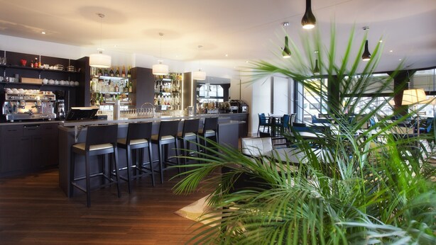 A modern bar area with a long counter, bar stools, and a variety of bottles and glasses on shelves. - Le Berry (Saint-Nazaire)