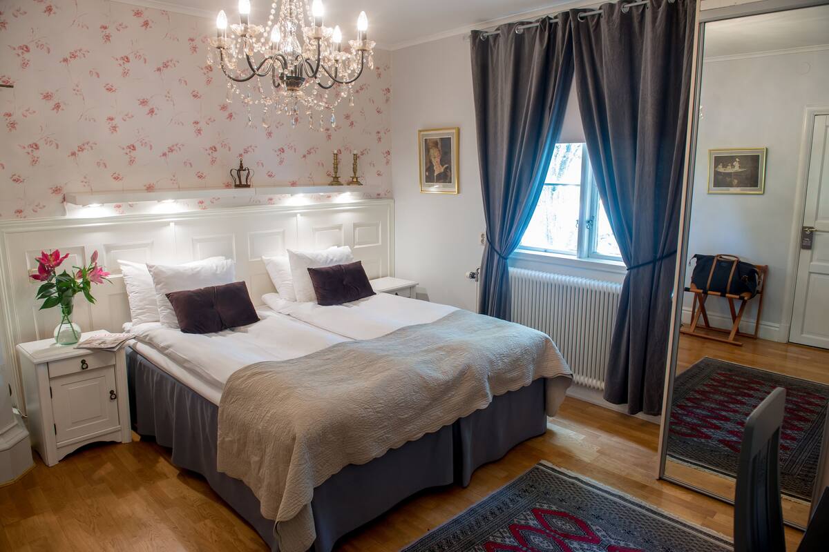 A bedroom with a large bed, a nightstand, a mirror, and a chandelier.