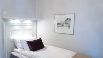 A neatly made bed with white linens and a brown pillow, a framed black and white photo on the wall, and a white headboard with built-in lighting.