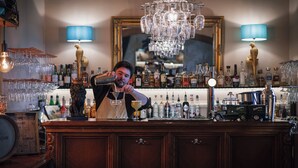 A bar area with a bartender, shelves of liquor bottles, a chandelier, and a mirror. - Slottshotellet i Kalmar (Kalmar)