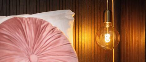 A bed with a pink pillow and a table lamp with a visible light bulb.