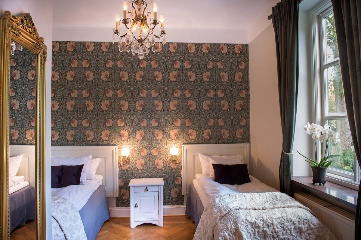 A bedroom with two beds, a nightstand, a chandelier, and a window with curtains.