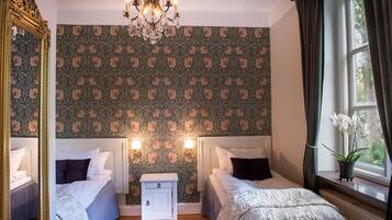A bedroom with two beds, a nightstand, a chandelier, and a window with curtains.