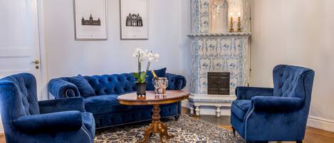 A room with a blue sofa set, a round wooden table with a vase and glasses, and a patterned rug.