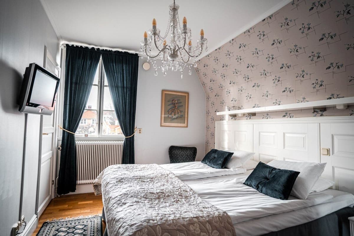 A bedroom with a bed, a chandelier, a radiator, a television, and a window with curtains.