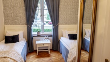 A bedroom with two beds, a small table with items, a window with curtains, and a mirror.