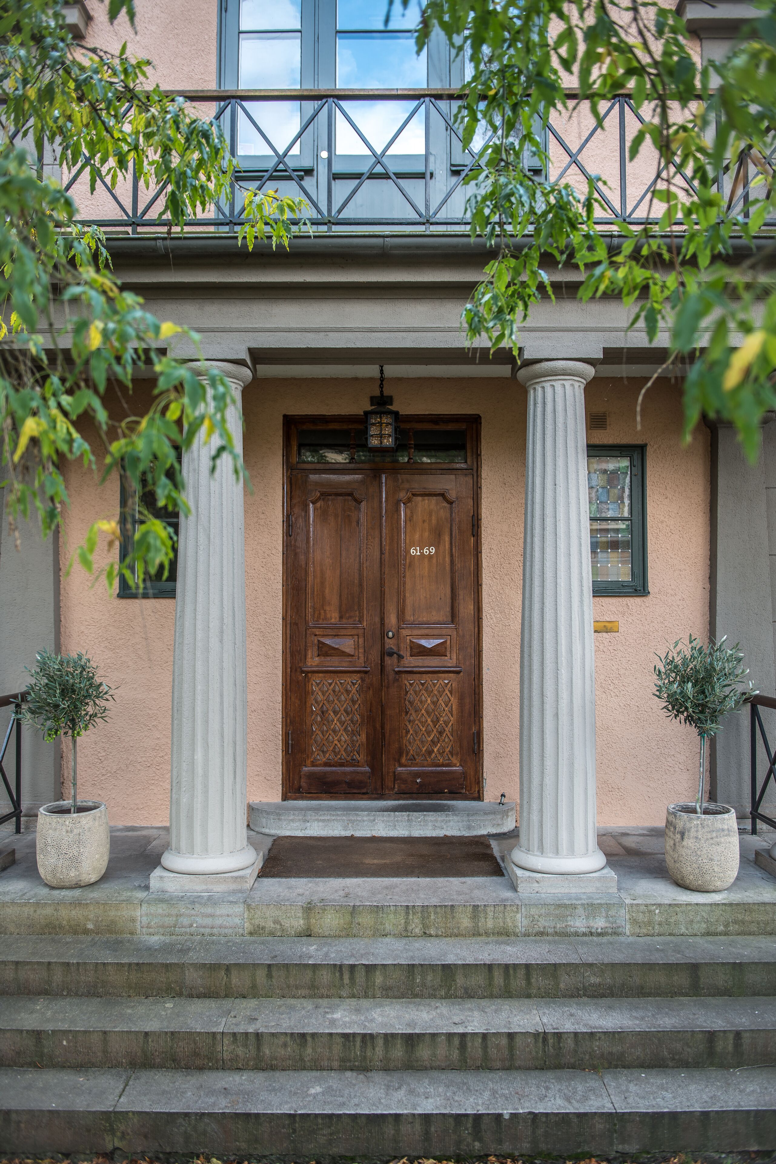 A building entrance with a wooden double door, two white columns, and a small window above the door.