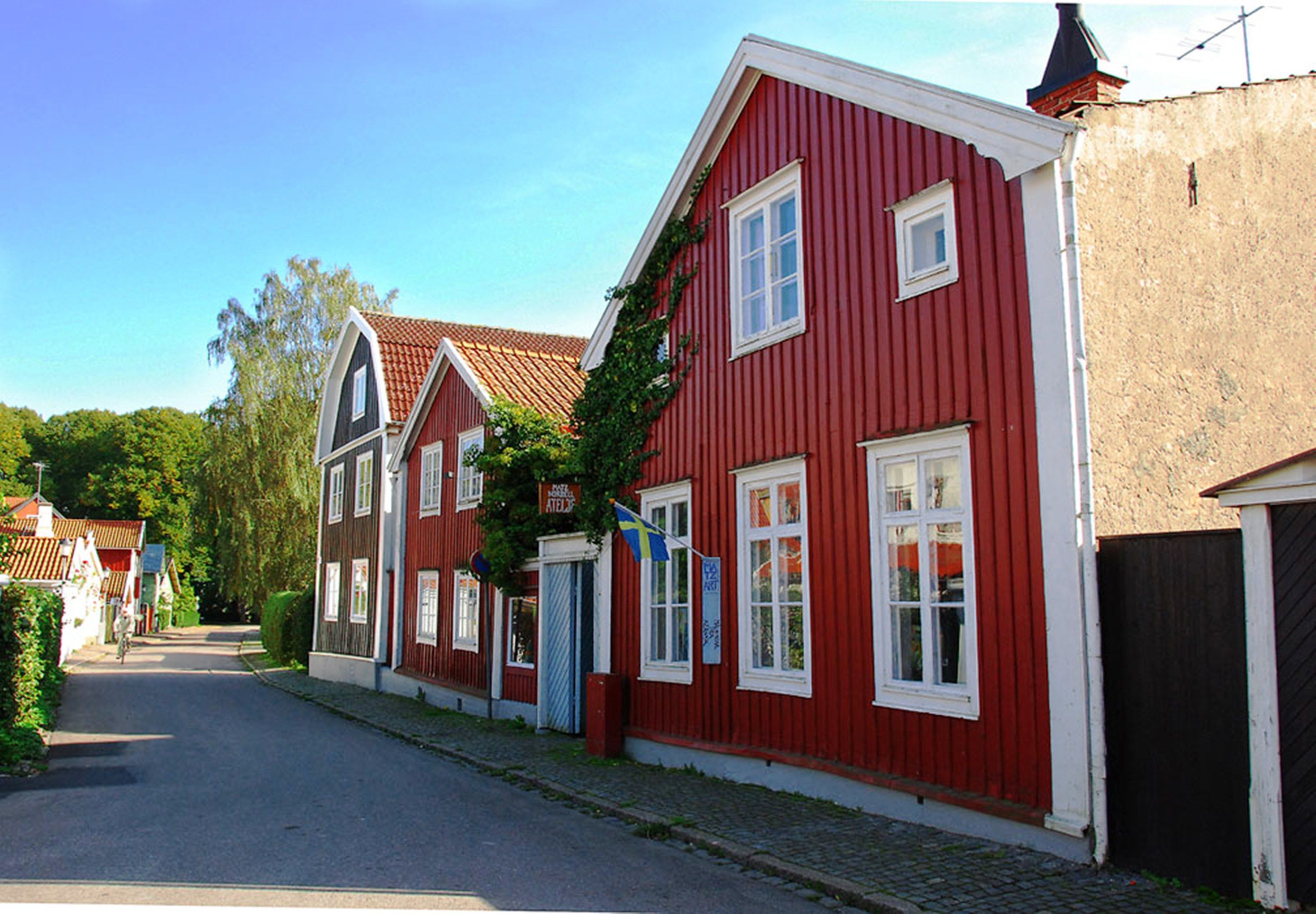 A row of red wooden houses with white trim, a cobblestone street, and a clear blue sky.