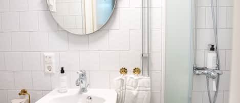 Un baño con lavamanos blanco, un espejo, toallero y ducha.
