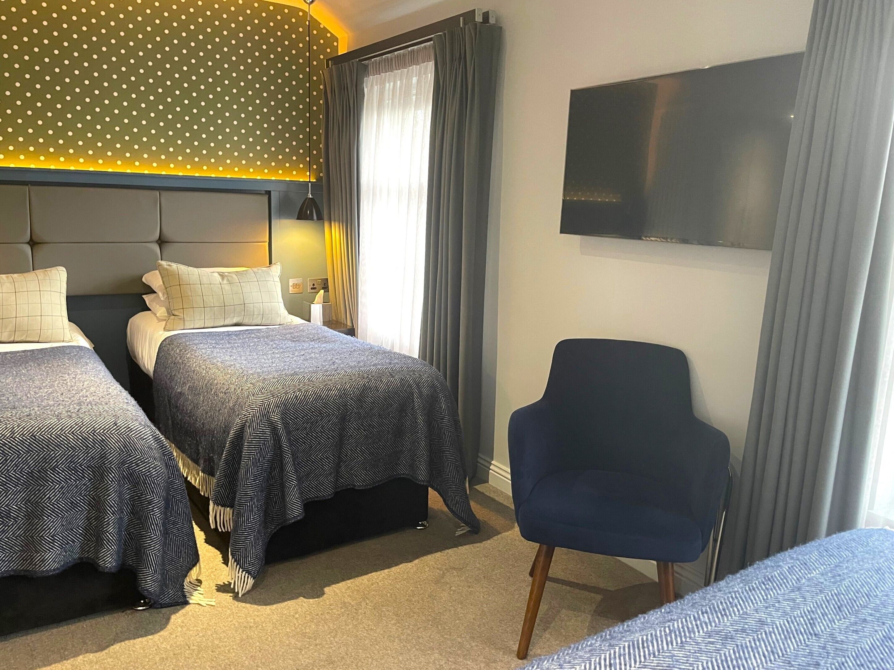 A hotel room with two beds, a TV, a chair, and a window with curtains.