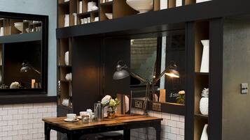 Een bar met een donker houten tafel, drie krukken en planken vol witte keramieken schalen.