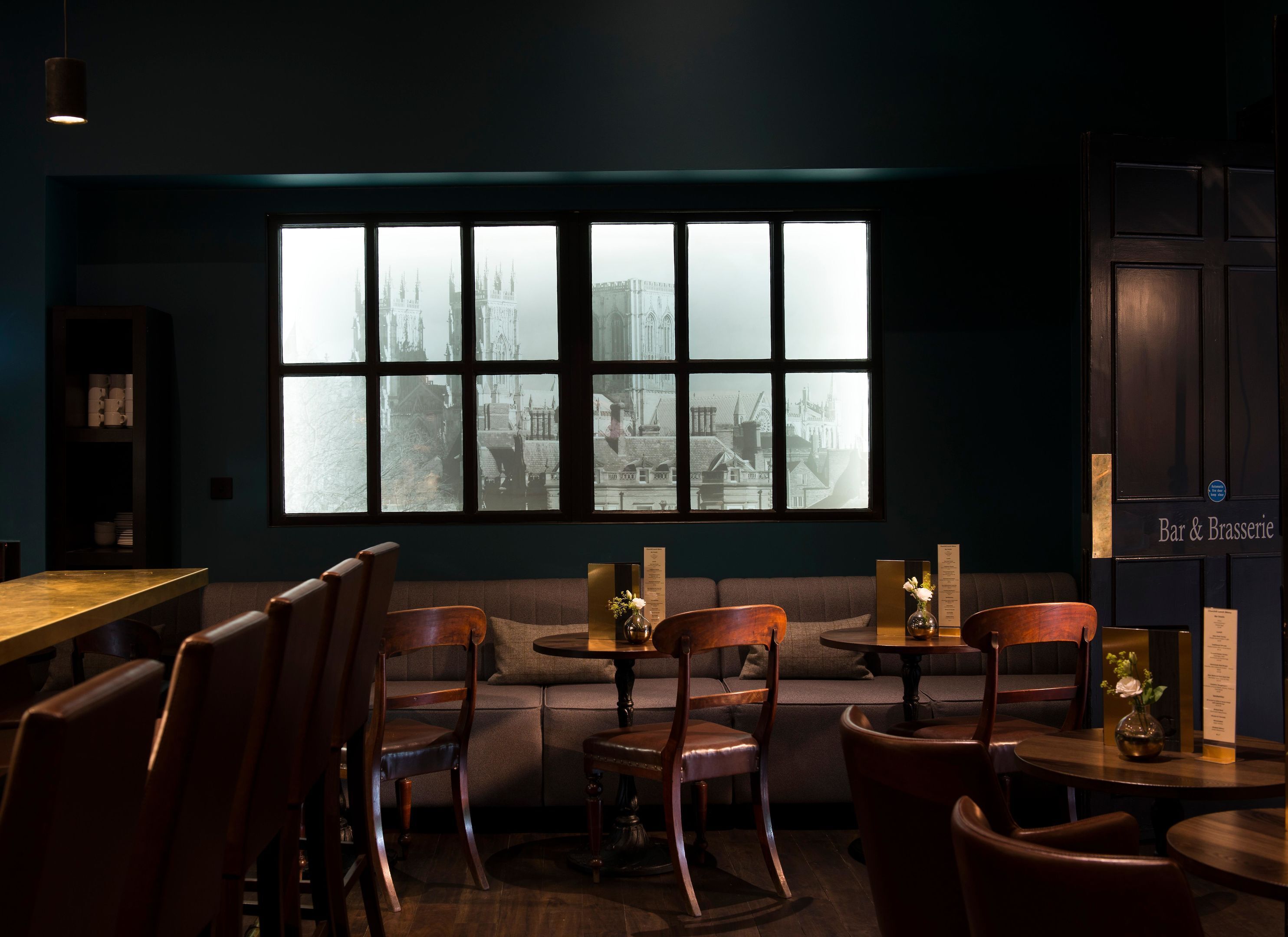 A cozy seating area with a large window overlooking a cityscape, wooden furniture, and a menu board on the wall.